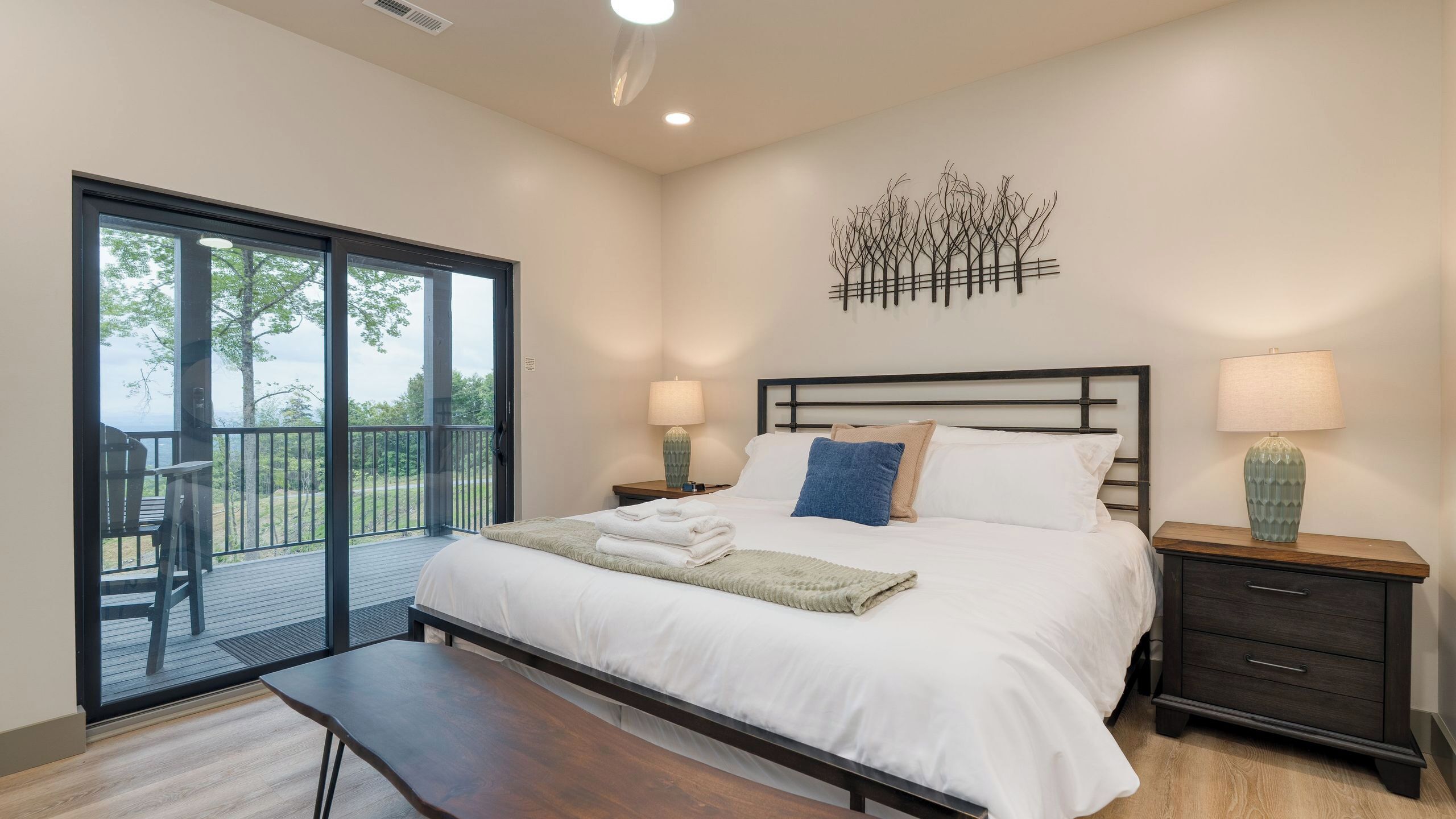 Un dormitorio con cama, mesitas de noche, un banco, un balcón con vistas y un adorno en la pared.