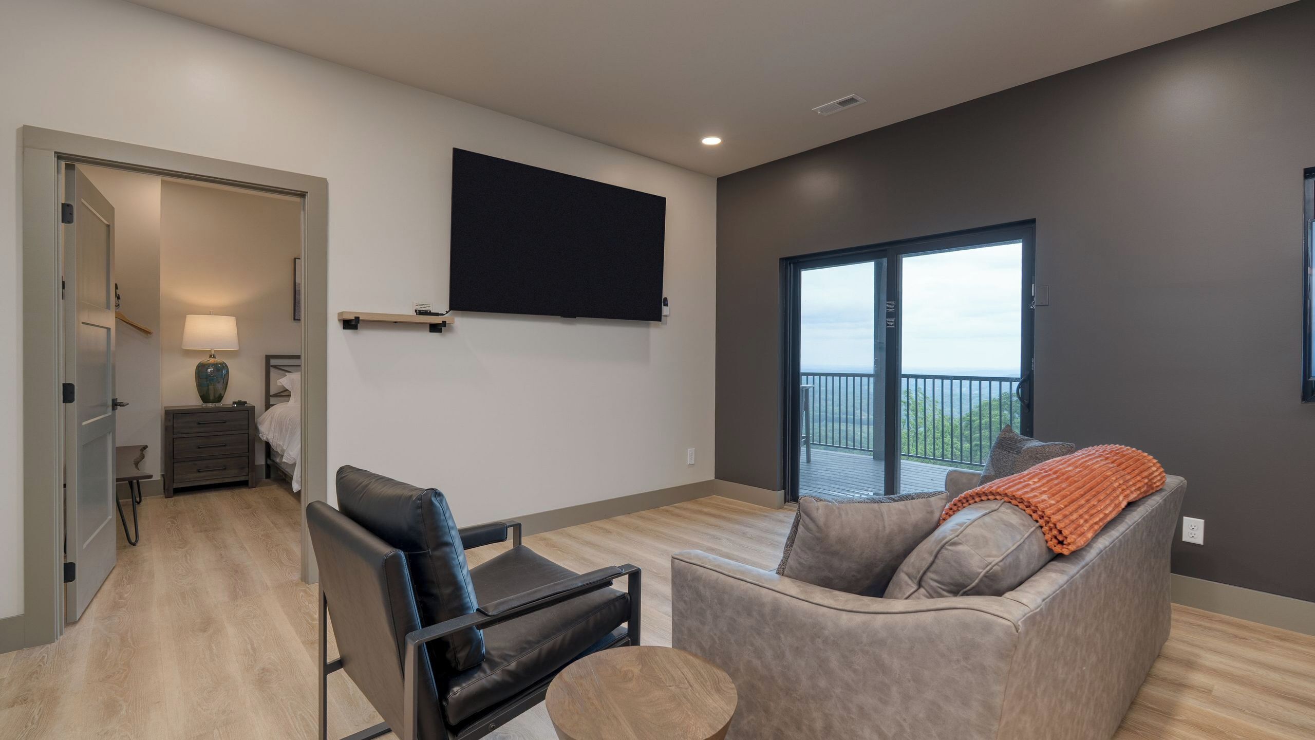 A modern living room with a sofa, a chair, a TV, and a balcony with a view.