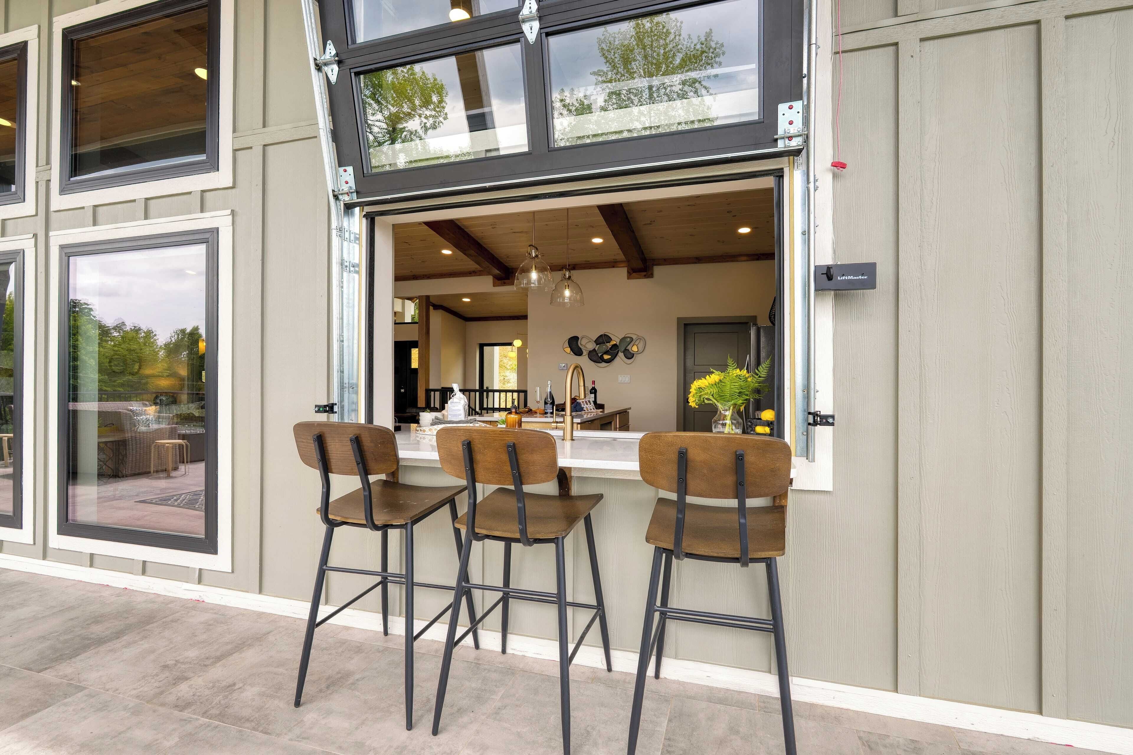 An outdoor bar area with three stools and a counter, large windows, and a view of the interior.