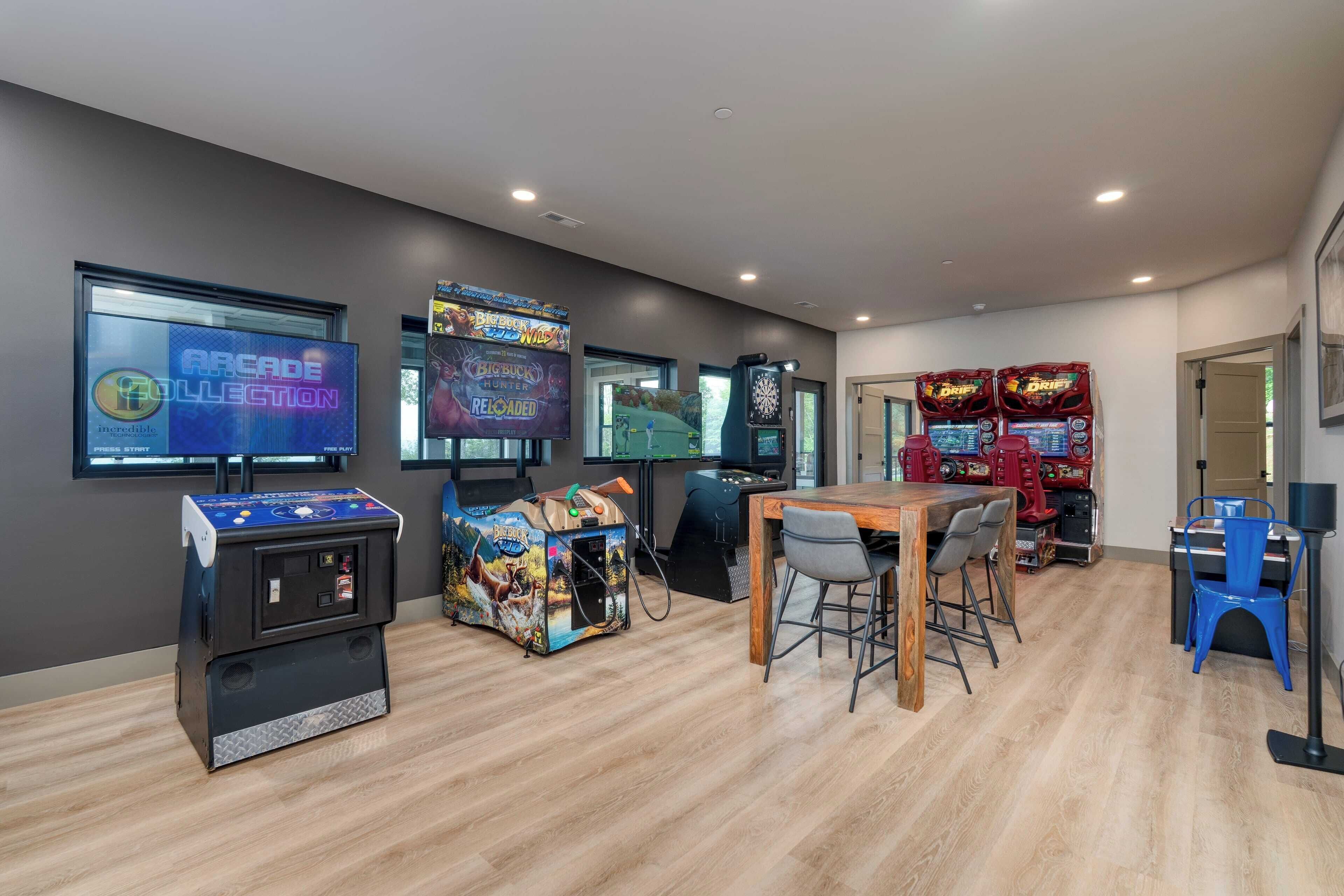 A room with arcade games, a table with chairs, and a television displaying game titles.