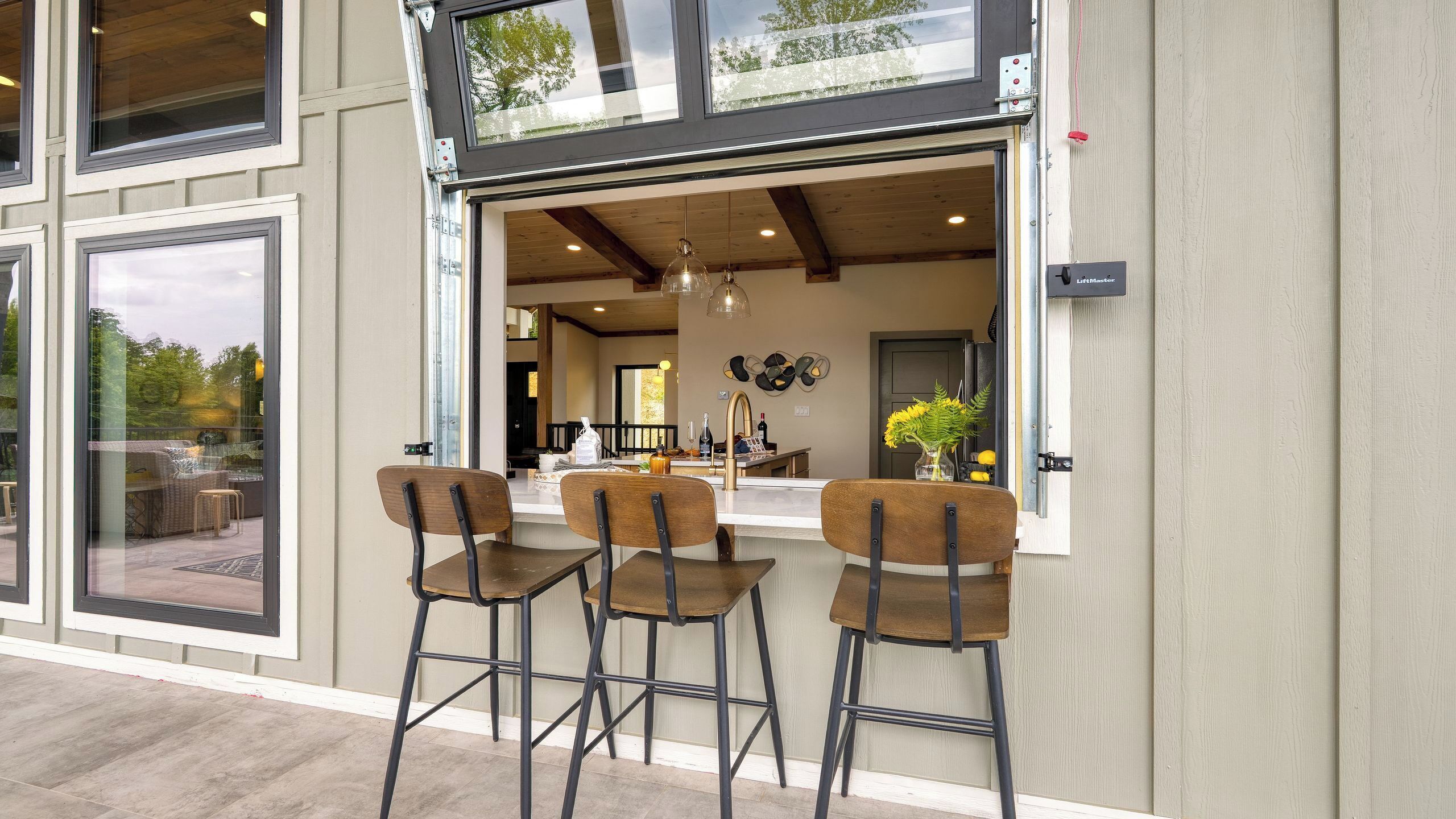 A modern bar area with three stools, a counter, and a view into the interior.