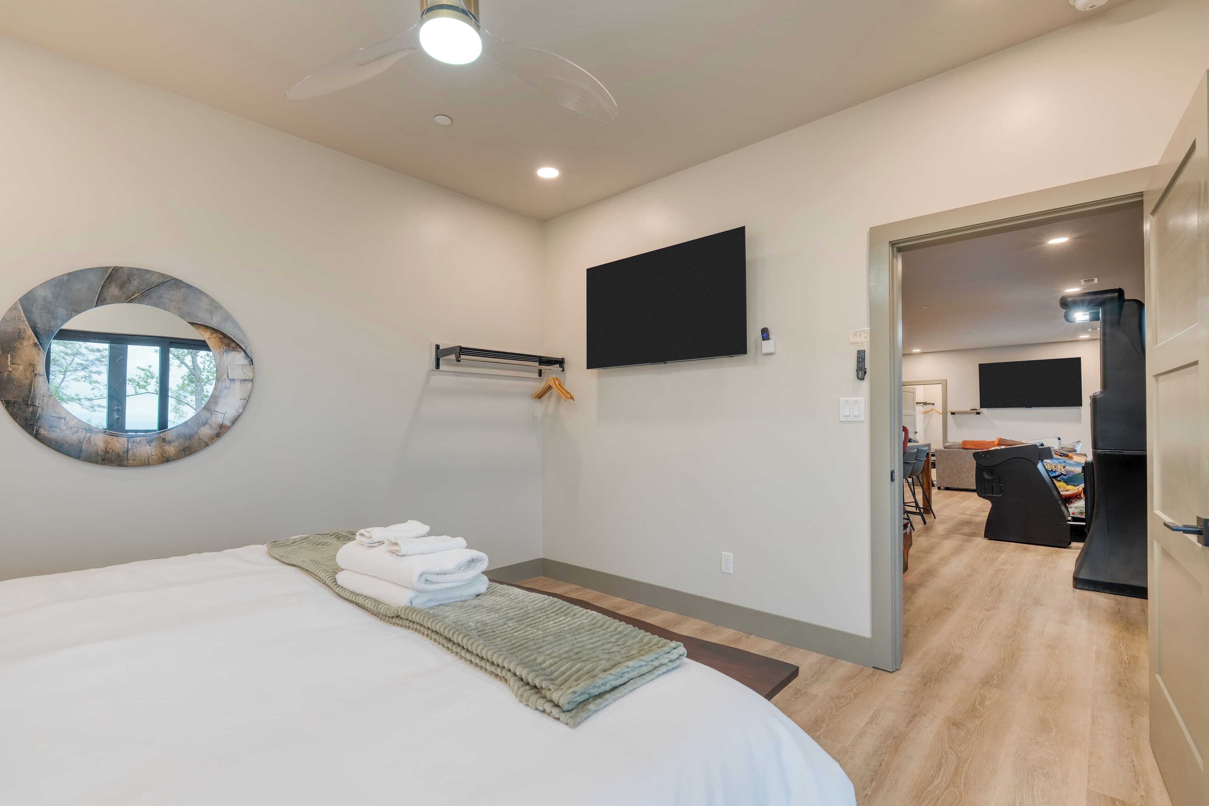 A modern bedroom with a bed, a round mirror, a flat-screen TV, and a wooden floor.