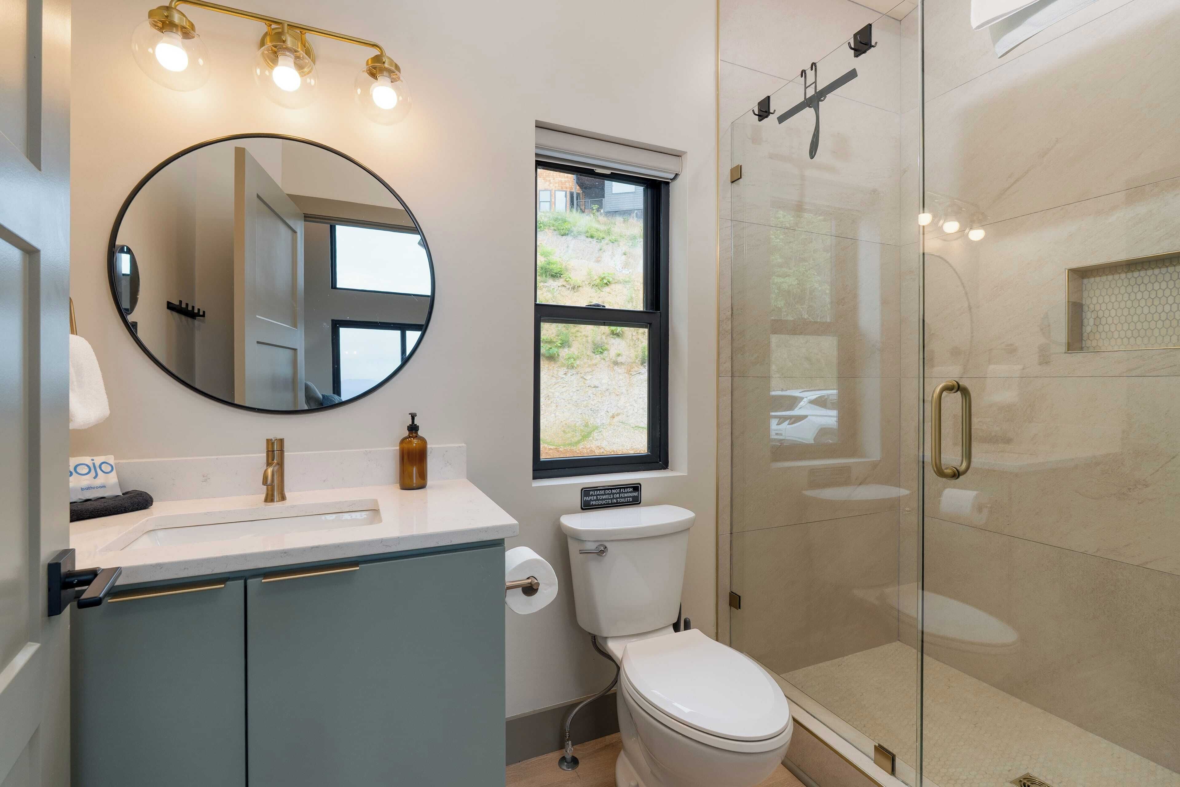 Une salle de bain moderne avec un grand miroir rond, des toilettes, un lavabo et une douche à parois de verre.
