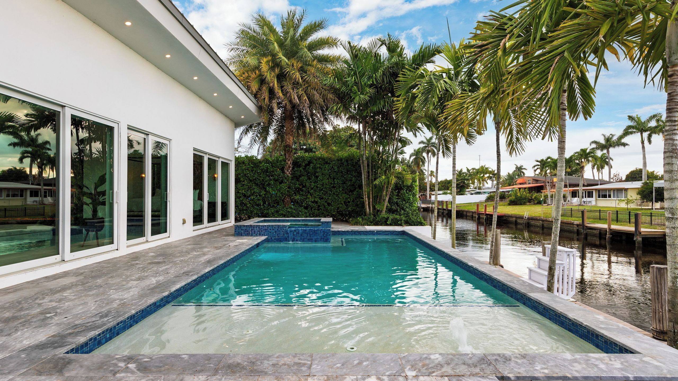 A swimming pool with a clear blue water feature, surrounded by palm trees and a modern building with large windows.