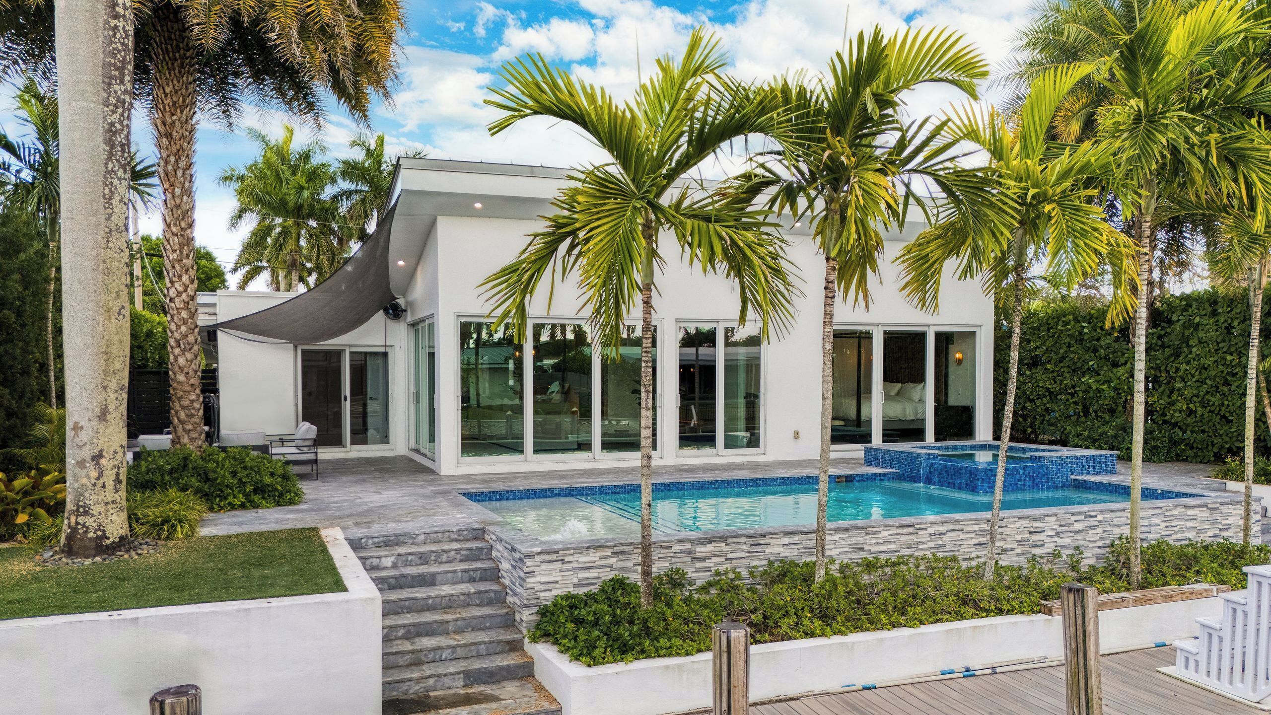 A modern house with a swimming pool, palm trees, and a patio area.