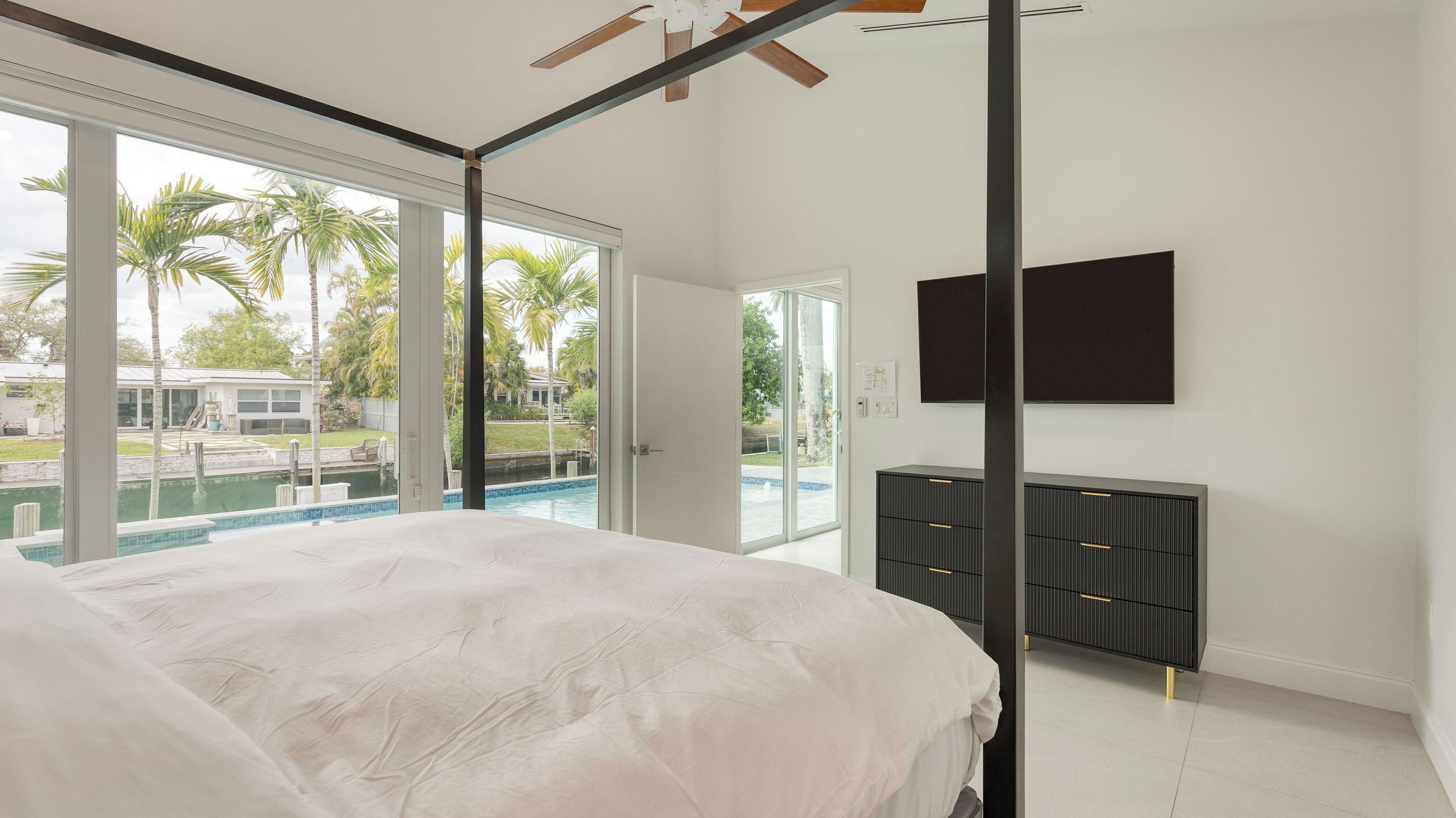 Un dormitorio con una cama grande, un televisor montado en la pared y vistas a una piscina.