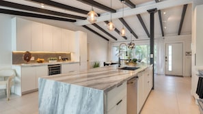 A modern kitchen with a marble island, pendant lighting, and a view of the outdoors. - Luxury Waterfront Home w/ Pool, Hot Tub & Dock Near Las Olas Gulfstream (Fort Lauderdale)