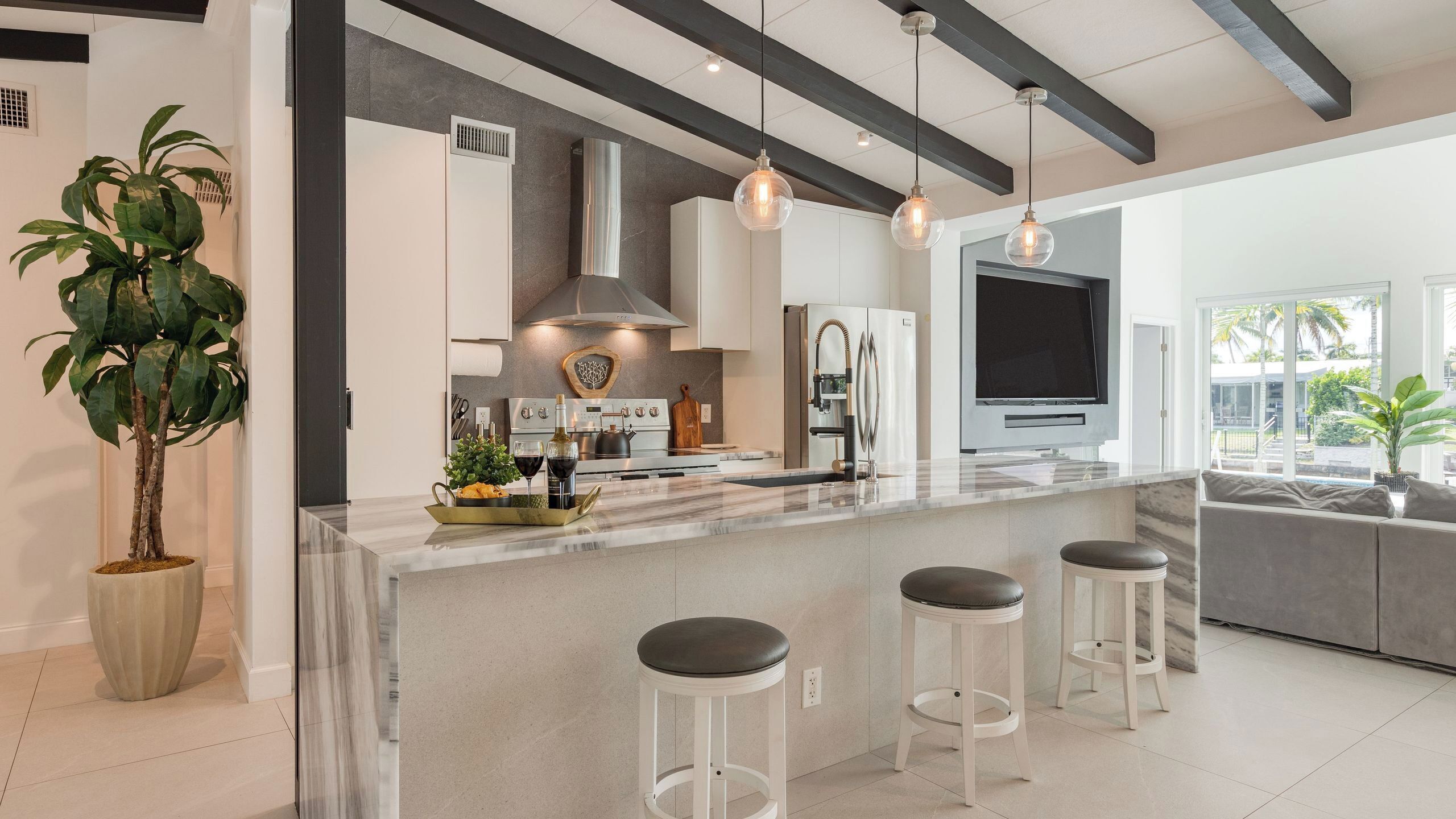 A modern kitchen with a marble countertop, stainless steel appliances, pendant lighting, and a large window.