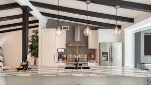 A modern kitchen with a marble island, stainless steel appliances, pendant lighting, and a black ceiling beam design. - Luxury Waterfront Home w/ Pool, Hot Tub & Dock Near Las Olas Gulfstream (Fort Lauderdale)