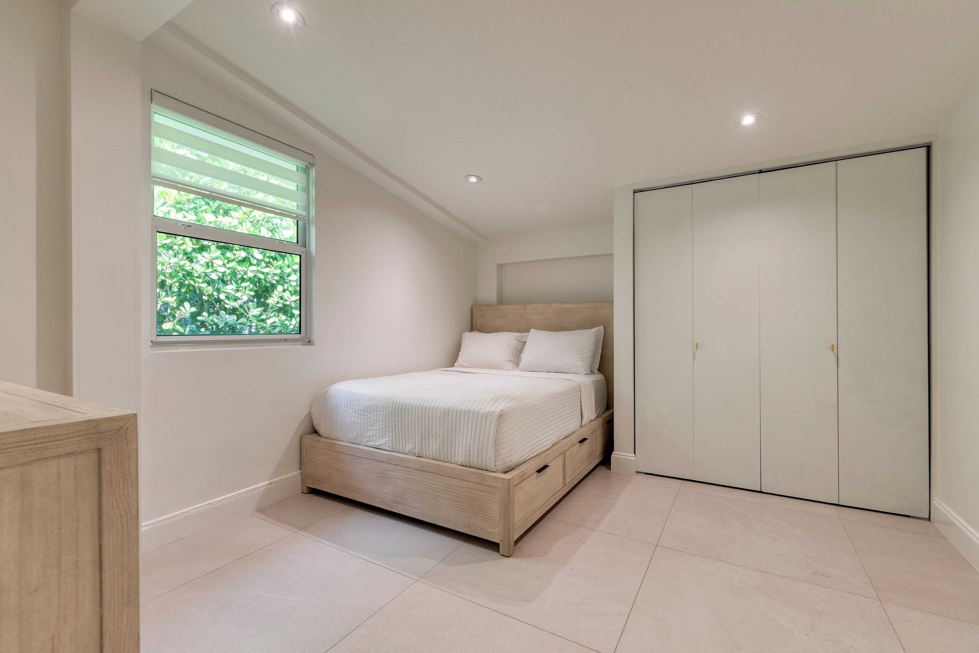 Une chambre à coucher avec un lit, une fenêtre avec des stores, une armoire et un meuble.