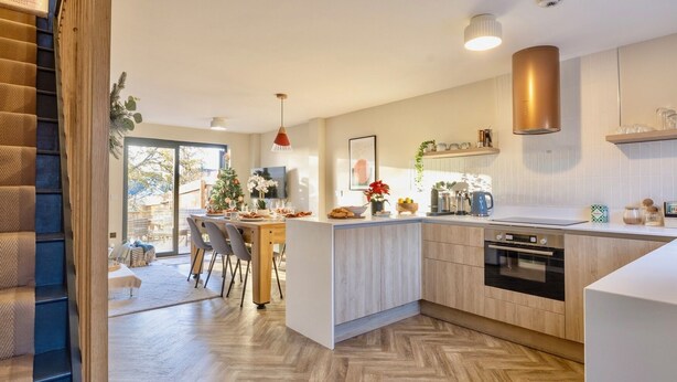 Una cucina moderna con isola centrale, pavimento in legno e zona pranzo con sedie.
