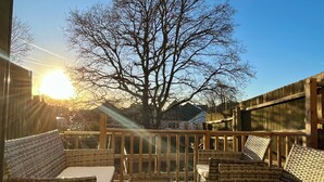 Una veranda esterna con mobili in vimini e un tavolo in vetro, circondata da un pontile di legno e un grande albero.