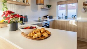Una cucina moderna con un piano di lavoro bianco, una ciotola di frutta e un piatto di croissant.