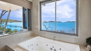 A modern bathroom with a large bathtub, a window with a view of the sea, and a balcony with a railing. - Hidden Cove 2 - 4 Bedroom, 4 Bathrooms, Waterfront with Private Pool and buggy (Hamilton Island)