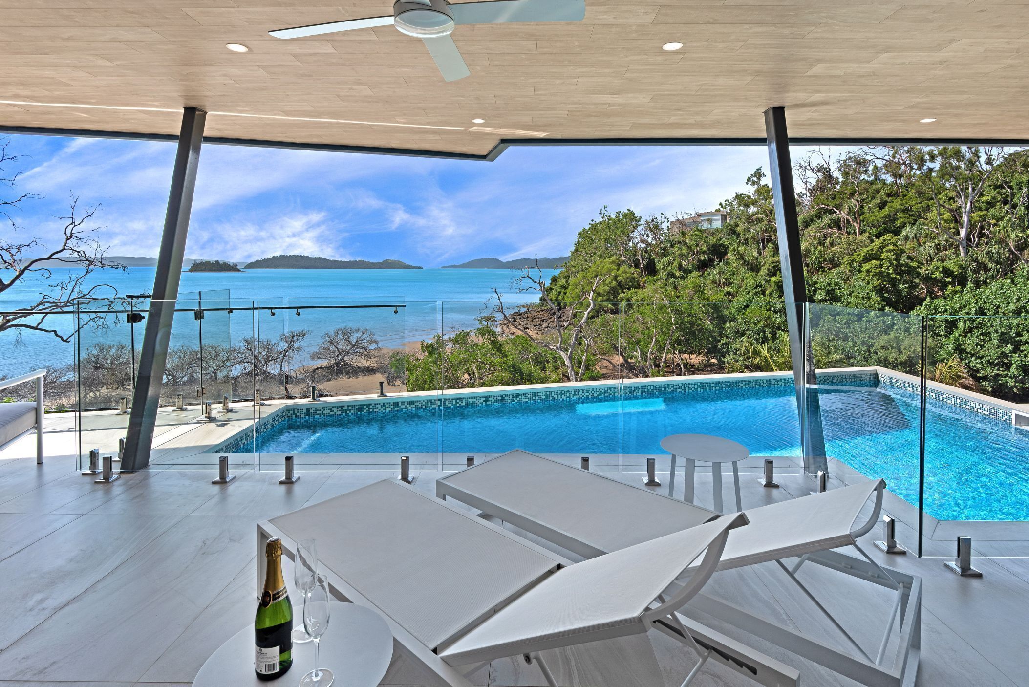 Un espace piscine extérieur moderne, avec une eau d’un bleu limpide, des chaises longues et une bouteille de champagne.