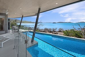 A modern infinity pool with clear blue water, a glass railing, and a view of the ocean and distant islands. - Hidden Cove 2 - 4 Bedroom, 4 Bathrooms, Waterfront with Private Pool and buggy (Hamilton Island)