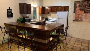 Eine Küche mit einer zentralen Kochinsel, dunklen Holzschränken, einem weißen Kühlschrank und einem Fliesenboden.