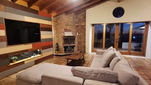 Ein gemütliches Wohnzimmer mit Kamin, einem großen Fernseher und einer Schiebetür zu einem Außenbereich.