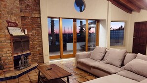 Ein Wohnzimmer mit Kamin aus Backstein, einer Couch und Blick auf den Strand bei Sonnenuntergang.