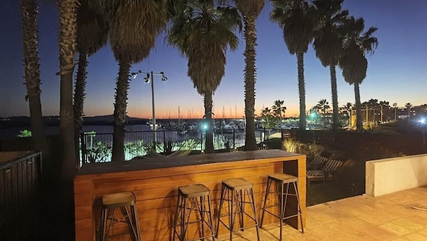 Eine Bar mit Holzhockern und Blick auf die Stadt bei Dämmerung.