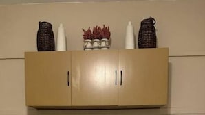 A laundry area with a washing machine and dryer, a wooden cabinet above, and a small shelf with decorative items.