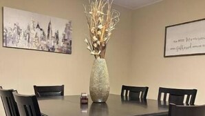 A conference room with a dark wooden table and chairs, a vase with dried plants, and two framed pictures on the walls.