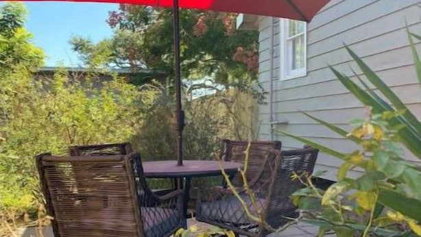 An outdoor patio with a table and chairs, a red umbrella, and a house in the background.