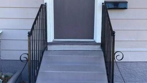 A front view of a house with a grey door, a small porch with a black railing, and a window to the right.