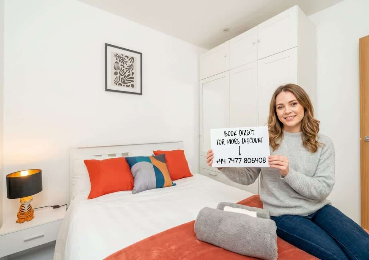 Una camera d'albergo con un letto, un comodino, una lampada, un quadro appeso alla parete e una persona che tiene un cartello.