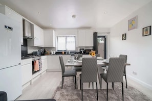 A modern kitchen with white cabinets, a dining area with a table and chairs, and a small window. - Comfy 3BR House | Near Tottenham Stadium | Parking (London)