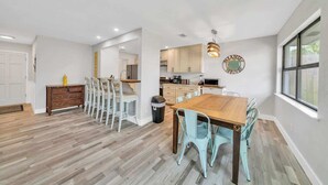 Una cocina moderna con armarios de madera, un comedor con mesa de madera y sillas azul claro, y un ventanal que proporciona luz natural.
