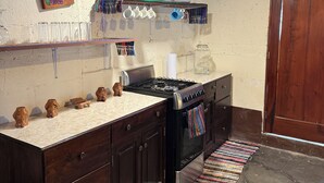 A kitchen with dark wooden cabinets, a gas stove, and a hanging rack with dishes.