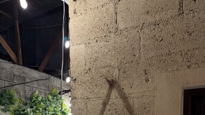 A rustic interior with a brick wall, a wooden sign with beverage options, and a potted plant.