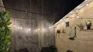 An outdoor patio area with brick flooring, wicker chairs, and string lights.