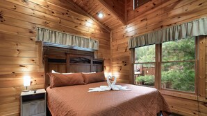 Un dormitorio de cabaña de madera con cama, mesita de noche y ventana con cortinas.