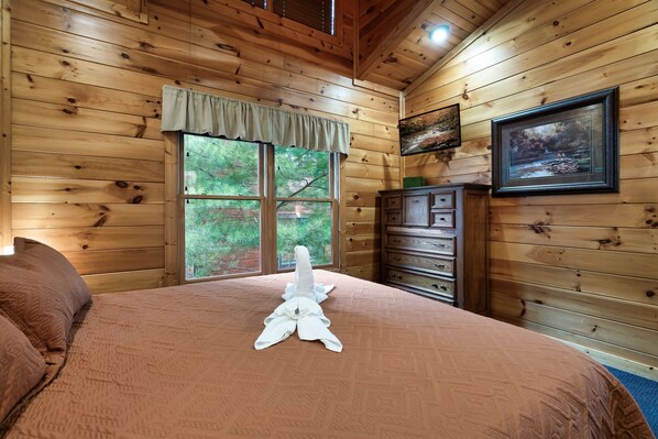 Een houten slaapkamer met een groot bed, een dressoir en een raam met uitzicht op bomen.