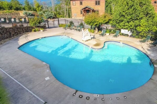 A large, curved swimming pool with a stone wall and lounge chairs around it.