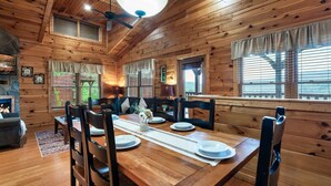 Interior de una cabaña de madera con una mesa de comedor dispuesta para cuatro personas, rodeada de sillas de madera.