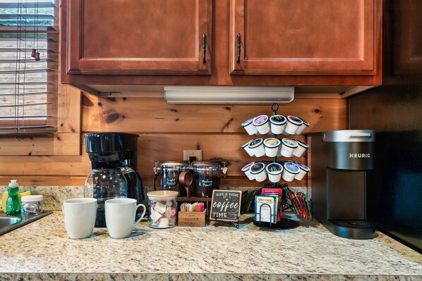 Una cocina con armarios de madera, una cafetera, tazas y una zona para preparar café.