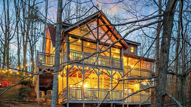 A multi-story wooden cabin with a balcony, surrounded by trees and a gravel path. - Sleeps 13 | Pet-Friendly, Hot Tub, Sauna & Theater (Sevierville)
