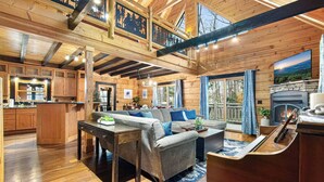 A spacious living area with a wooden interior, a fireplace, and a large window overlooking a scenic view. - Sleeps 13 | Pet-Friendly, Hot Tub, Sauna & Theater (Sevierville)