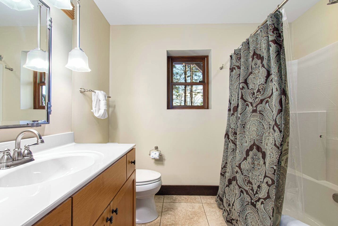 A bathroom with a white sink, wooden cabinet, and a shower curtain with a paisley pattern.
