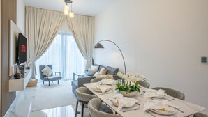 Ein modernes Wohnzimmer mit Essbereich, einem Flachbildfernseher und einem großen Fenster mit Vorhängen.