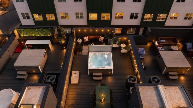 Un patio en la azotea con jacuzzi, zonas de estar y luces colgantes.
