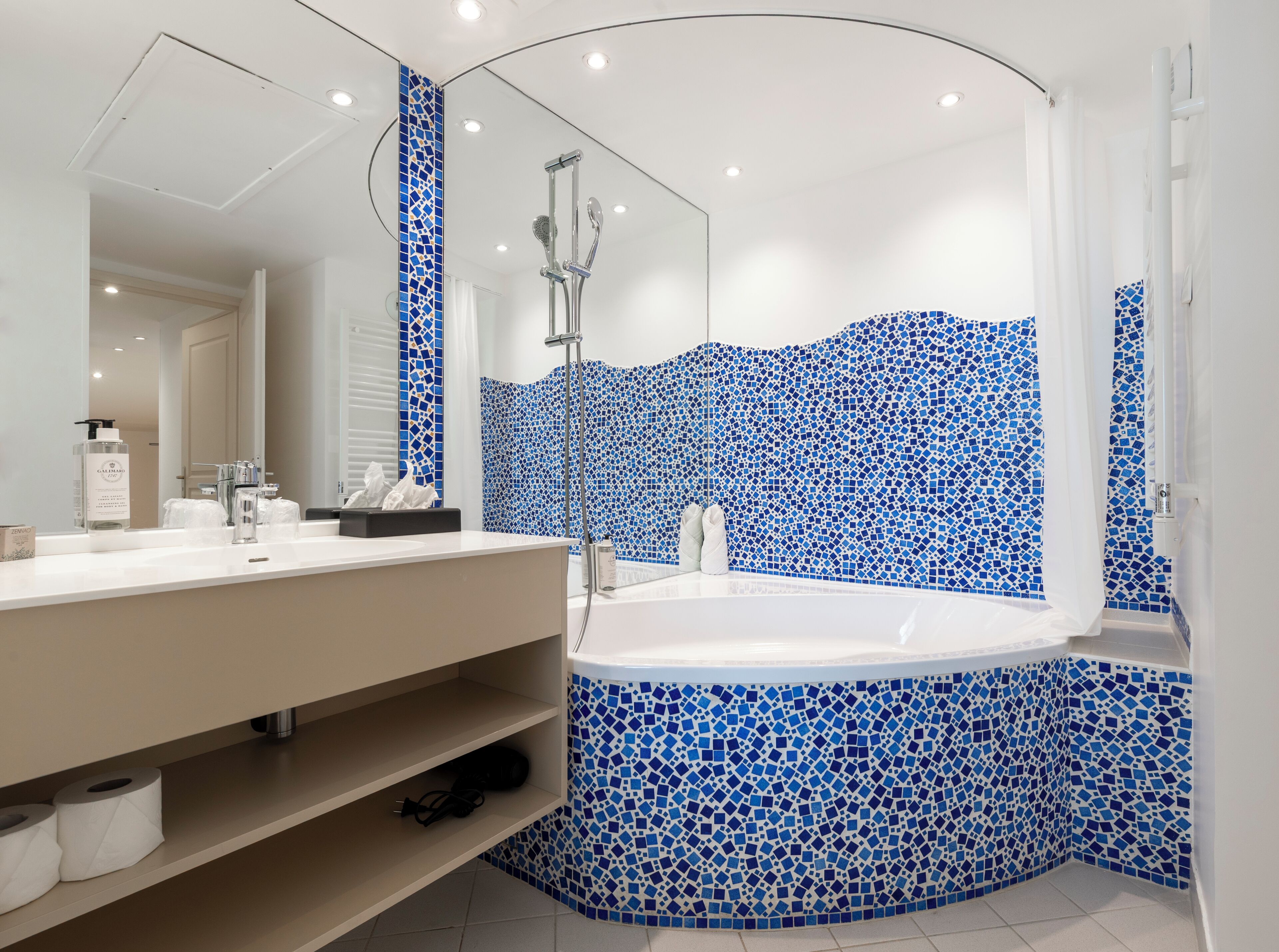 Une salle de bain moderne avec un meuble-lavabo blanc, une grande baignoire et des murs recouverts de mosaïques bleues.