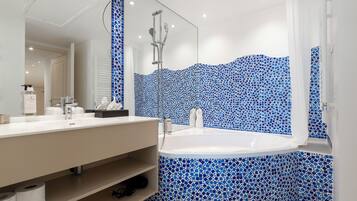 A modern bathroom with a white vanity, a large bathtub, and blue mosaic tile walls.