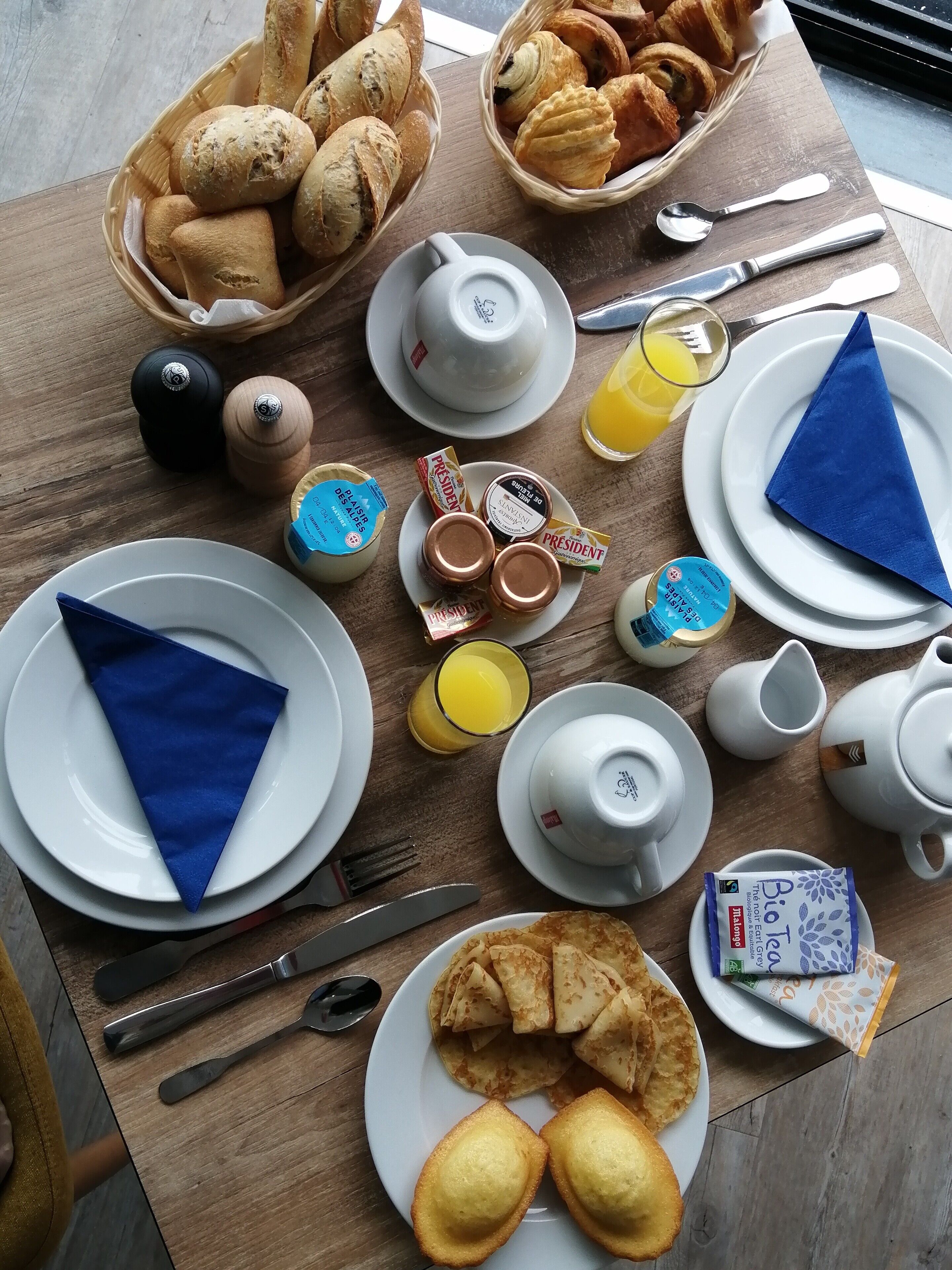 Una mesa de desayuno con cruasanes, pastelería y una variedad de untables y condimentos.