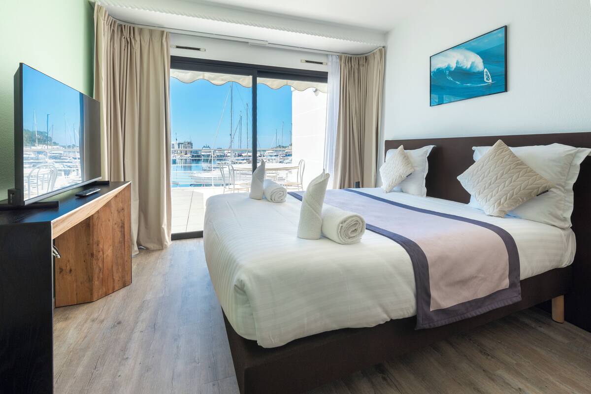 Una habitación de hotel con una cama grande, televisión y vistas al puerto deportivo.