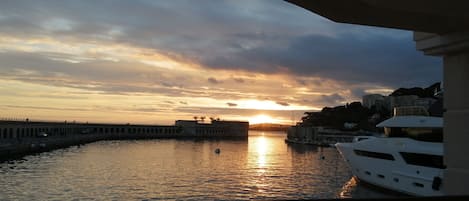A sunset view from a balcony overlooking a marina with boats and a distant cityscape.