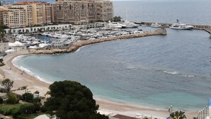 A coastal marina with yachts docked, a beach, and a large hotel building in the background.